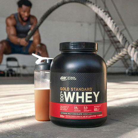 Man working out behind bottle of Optimum Nutrition Gold Standard 100% Whey Protein Extreme Milk Chocolate